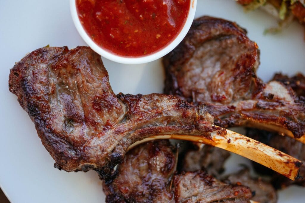 Sočni janjeći kotleti s roštilja prikazani na rešetki uz aromatične začine, idealni za ukusno i mirisno BBQ uživanje.